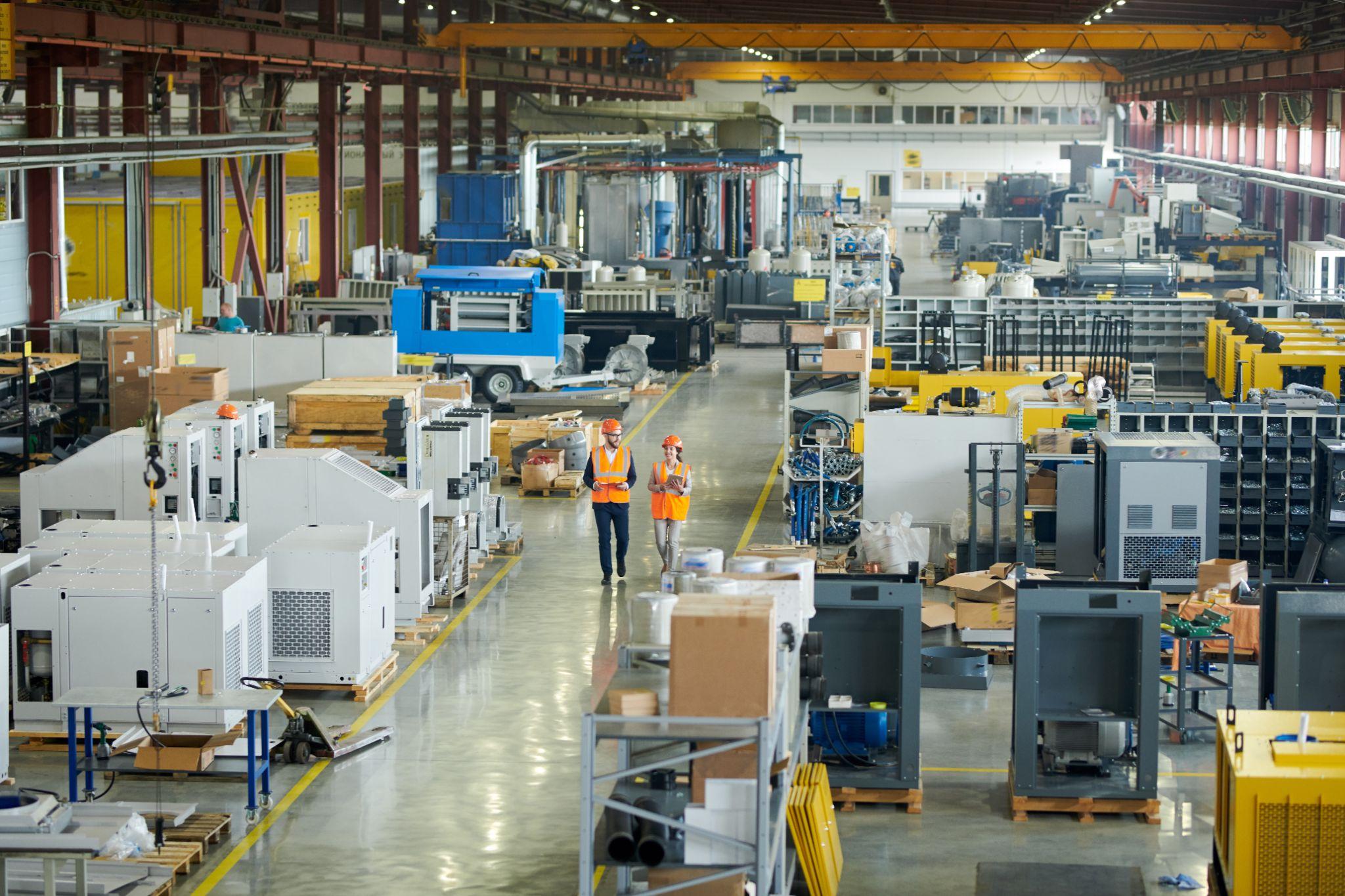 Businessman wearing hardhat walking across production workshop accompanied