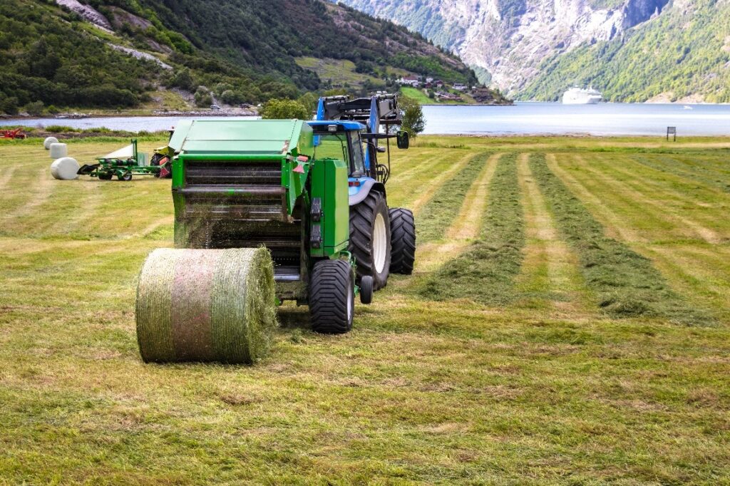 small-tractor-with-round-baler unloading on a field in Geiranger