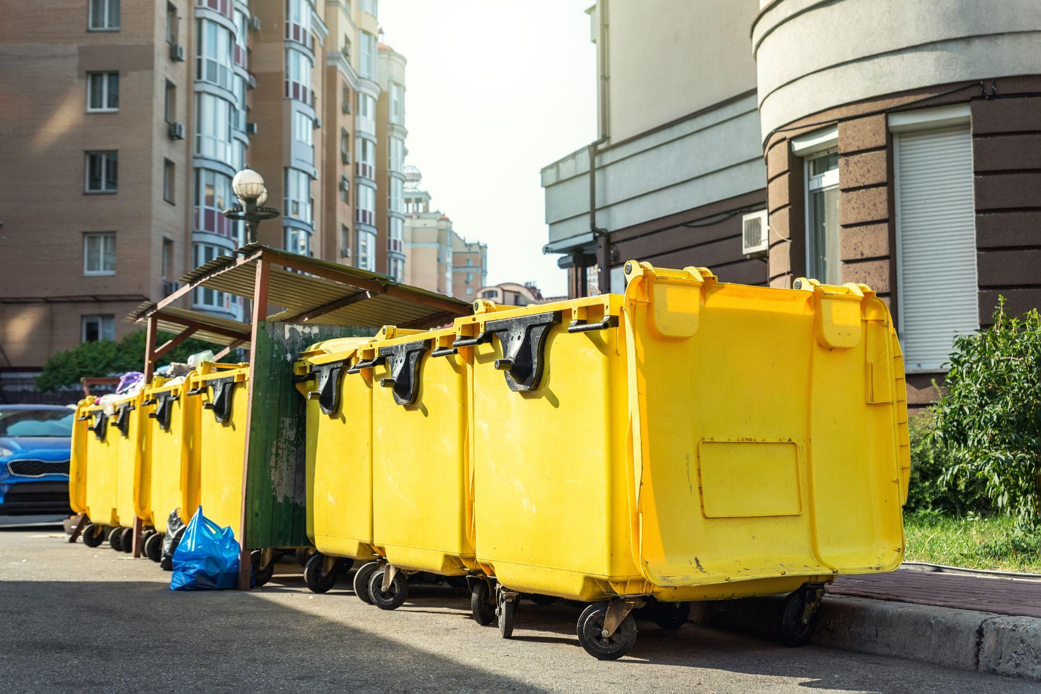 Rows of many big plastic yellow dumpster cans near residential building