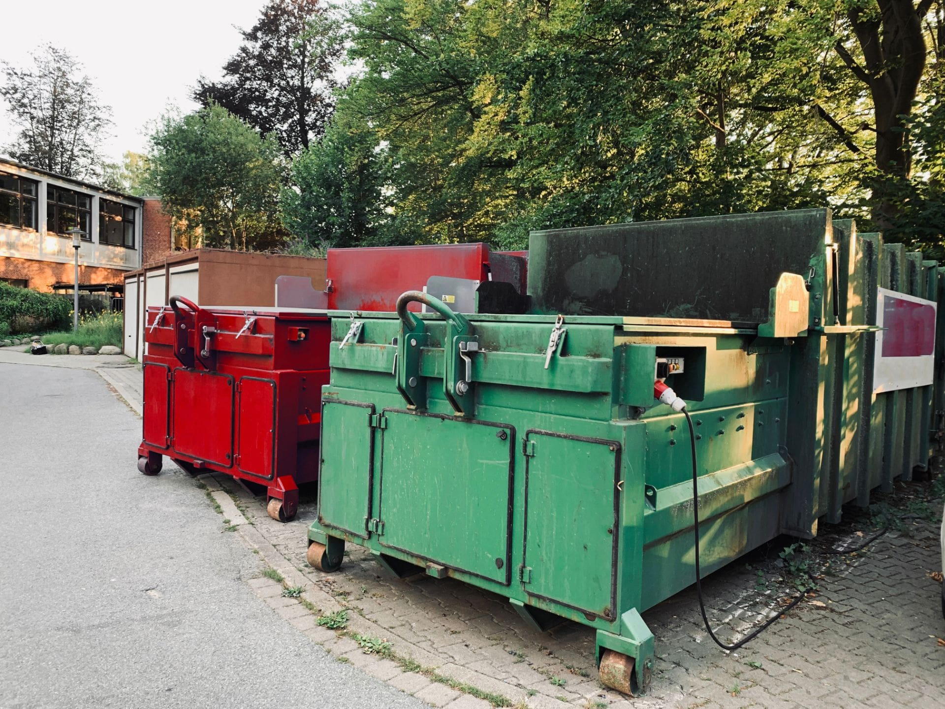 on an industrial site a green waste compactor and a red waste compactor stand side by side